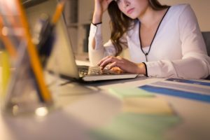 A woman sitting at a desk looking at a laptop.