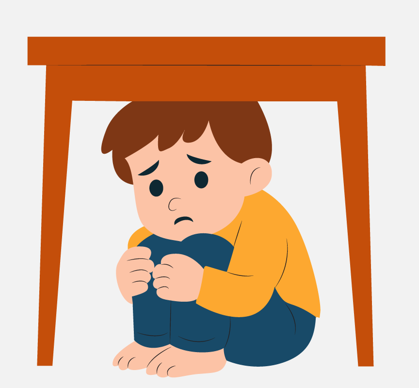 A scared, young boy hiding under a table with his knees to his chest.