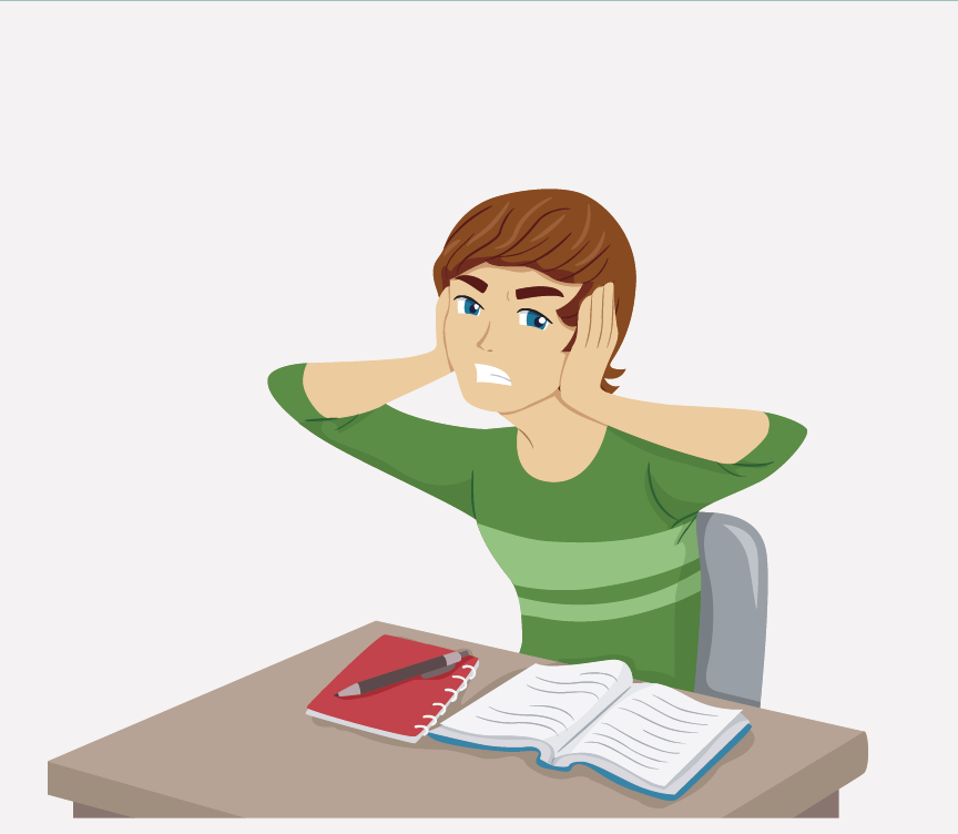 A boy sitting at a school desk with his hands on his head.