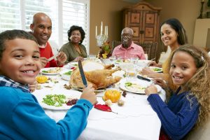 A family is sitting at a table. They are smiling as they eat their dinner.