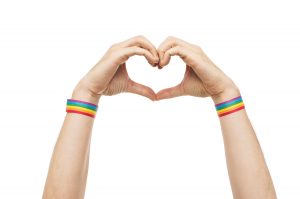 Two hands making a heart. They have rainbow wristbands
