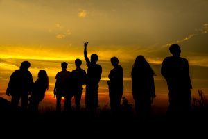 Group of peoples' silhouettes standing in front of a sunset.
