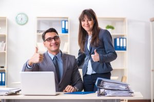A working man and woman are by a computer giving a thumbs up
