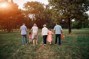 Rear view of three generation family walking in a park. They are looking for some nice place for family weekend picnic. Holding hands and walking threw the grass. Grandfather is holding basket with food and drink.
